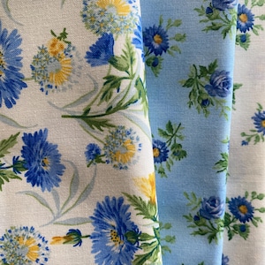 以下が含まれることがあります： 花柄の3つの生地のクローズアップ。最初の生地は、青と黄色の花と緑の葉が付いた白です。2番目の生地は、青い花と緑の葉が付いた水色です。3番目の生地は、青い花が付いた白です。