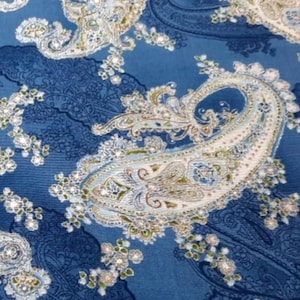 May include: Close-up of blue paisley fabric with white, green, and tan accents. The fabric features large paisley designs and smaller floral patterns. The text "for ROBERTKAUFMAN" is visible at the bottom.