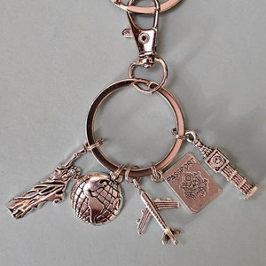 May include: Silver keychain with charms representing travel, including the Statue of Liberty, a globe, an airplane, a passport, and Big Ben.