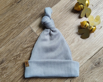 May include: A gray ribbed knit baby hat with a knotted top. The hat has a small brown leather tag with a logo on it.
