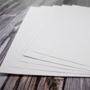 May include: Stack of white cardstock paper on a woodgrain surface.