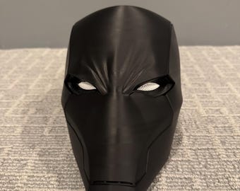 May include: A black superhero mask with white mesh eye coverings. The mask has a smooth, matte finish and is designed with sharp, angular lines. The mask is likely for cosplay or costume use.