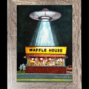 Puede incluir: Una pintura de acuarela de un OVNI sobrevolando un restaurante Waffle House. El OVNI est&aacute; emitiendo un rayo de luz. La pintura est&aacute; enmarcada en un marco de madera gris. La pintura mide 12,7x17,8 cm y est&aacute; firmada por el artista. El marco mide 16,5x21,6 cm.