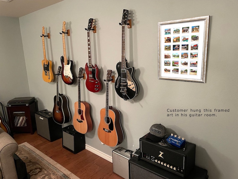 May include: A collection of electric and acoustic guitars mounted on a gray wall. The guitars are various colors, including natural wood, red, and black. A framed artwork with multiple small images hangs on the wall. The text in the image says, "Customer hung this framed art in his guitar room."