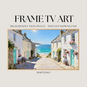 May include: A framed digital art print featuring a coastal village scene. White buildings with blue doors and flower boxes line a cobblestone street leading to the ocean. The text "FRAME TV ART" is at the top.