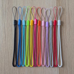 May include: A collection of twelve lanyard straps in various colours including black, blue, light blue, lime green, yellow, magenta, orange, light pink, lavender, grey, red, and white. Each strap features a braided cord and a plastic connector.