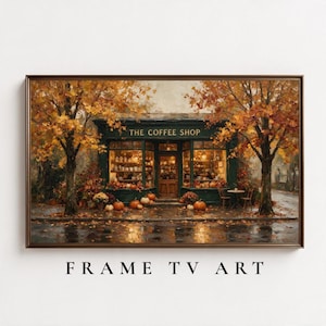Pode incluir: Uma impressão de arte paisagística emoldurada retratando a fachada de uma cafeteria com acabamento verde escuro e o texto THE COFFEE SHOP. A cena apresenta duas grandes árvores com folhagem de outono laranja, abóboras e reflexos na rua.