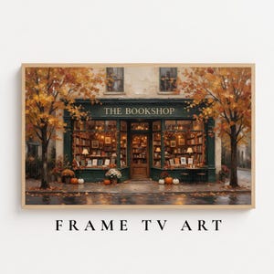 May include: A framed digital art print depicting a storefront labeled THE BOOKSHOP in dark green with large windows displaying bookshelves. The scene is framed by two trees with orange and yellow autumn leaves, with pumpkins placed on the sidewalk.