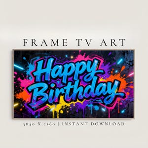 May include: A framed digital art print with the words "Happy Birthday" in a graffiti style. The artwork features a black background with neon blue, pink, orange, and yellow paint splatters. The text is in blue with a black outline.
