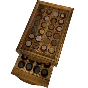 Peut inclure: Un présentoir à pièces en bois avec un dessus en verre et un tiroir coulissant. Le boîtier est rempli de diverses pièces de monnaie sur un fond de velours rouge. Le bois a une finition naturelle et chaleureuse, et les pièces varient en taille et en couleur.