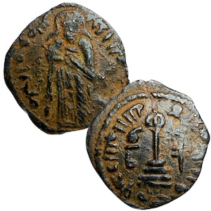 May include: Two antique bronze coins. One coin features a standing figure with a halo, the other shows a stylized design with text. The coins have a weathered appearance, with visible details and inscriptions.