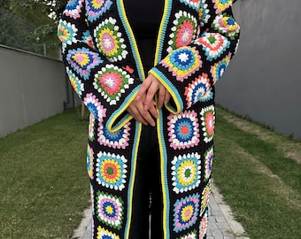 May include: A long, open-front crochet cardigan in a patchwork design. The cardigan features a black base with colorful squares in shades of pink, yellow, blue, and green. The edges are trimmed with yellow and blue. This handmade garment is a unique fashion statement.