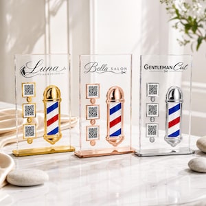 Könnte beinhalten: Drei transparente Acryl-Friseurladen-Pol-Displays. Jedes hat eine andere metallische Oberfläche: Gold, Roségold und Silber. Die Stangen haben rot, weiß und blaue Streifen. Jedes Display hat einen Salonnamen und QR-Codes.