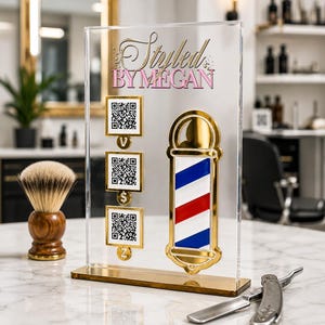 Puede incluir: Un letrero de acrílico transparente con detalles dorados, que muestra el texto "Styled BY MEGAN" en oro y rosa. Incluye un diseño de poste de barbero y tres códigos QR. También se ven una brocha de afeitar y una navaja.