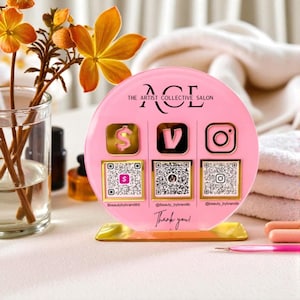 May include: A pink acrylic salon display with the text "ACE THE ARTIST COLLECTIVE SALON". It features icons for payment, video, and Instagram, each with a corresponding QR code. The base is gold, and the text "Thank you!" is at the bottom.