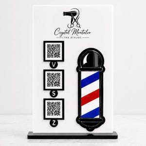 Könnte beinhalten: Ein weißes rechteckiges Schild mit einem schwarzen Logo aus Haartrockner und Schere, dem Text Crystal Montalvo THE STYLIST, drei schwarz umrandeten QR-Codes mit V-, S- und Z-Symbolen sowie einer vertikalen rot-weiß-blauen Barber-Pole-Grafik.