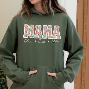 May include: An olive green hoodie with a floral "MAMA" design across the chest. The names "Olivia", "Sam", and "Mike" are printed below the word "MAMA". The hoodie has a kangaroo pocket and a drawstring hood.