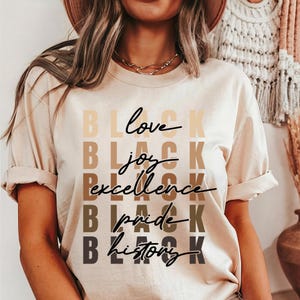 May include: A beige t-shirt with the words "Black love", "Black joy", "Black excellence", "Black pride", and "Black history" printed in black on the front.