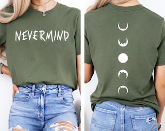 May include: Olive green t-shirt with the word "NEVERMIND" in white on the front. The back of the shirt features a vertical design of white moon phases. The shirt is paired with blue jeans.