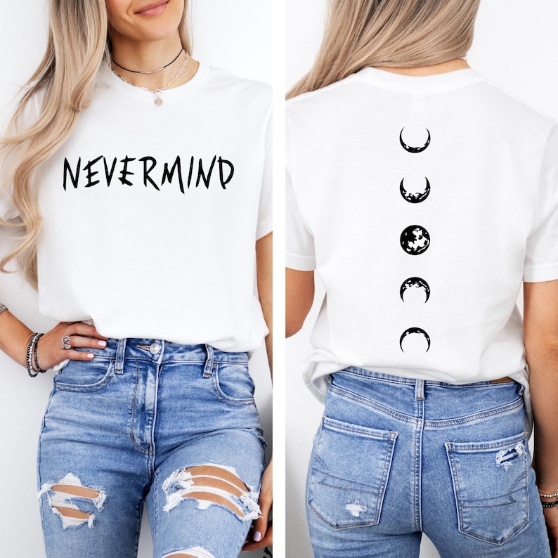 May include: White t-shirt with the word "NEVERMIND" in black script on the front. The back of the shirt features a black moon phase design. The shirt is paired with blue jeans.