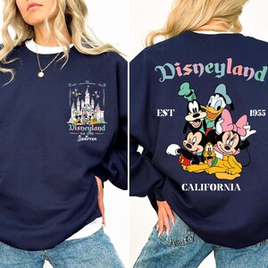 May include: A navy blue sweatshirt with a graphic print of Disneyland's castle and the text "Disneyland est 1955 Jennifer". The back of the sweatshirt has a graphic print of Mickey Mouse, Minnie Mouse, Goofy, Donald Duck, and Pluto with the text "Disneyland est 1955 California".