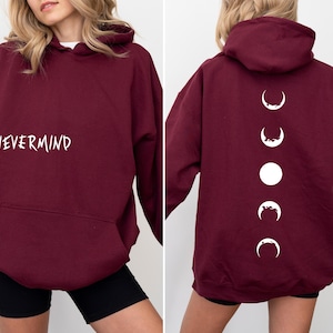 May include: A maroon hoodie with the word "NEVERMIND" in white script on the front. The back features a vertical design of white moon phases. The hoodie has a hood and a front pocket.