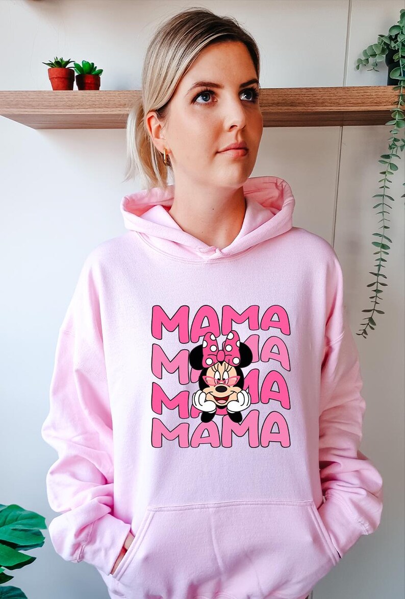 K&ouml;nnte beinhalten: Hellrosa Kapuzenpullover mit dem Wort "MAMA" in rosa Blockbuchstaben, viermal wiederholt. Eine Cartoon-Grafik von Minnie Mouse befindet sich unter dem Text. Die Figur tr&auml;gt eine Sonnenbrille und eine rosa Schleife.