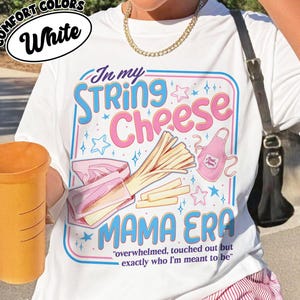 May include: White t-shirt with a colorful graphic that reads "In my String Cheese Mama Era." The design includes string cheese, stars, and an apron. The text "overwhelmed, touched out but exactly who I'm meant to be" is also included.