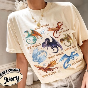 May include: Ivory-colored t-shirt featuring colorful dragon illustrations with text labels like "Rain Wings" and "Ice Wings." The shirt also has the text "Comfort Colors" and "Ivory" in a circular design.