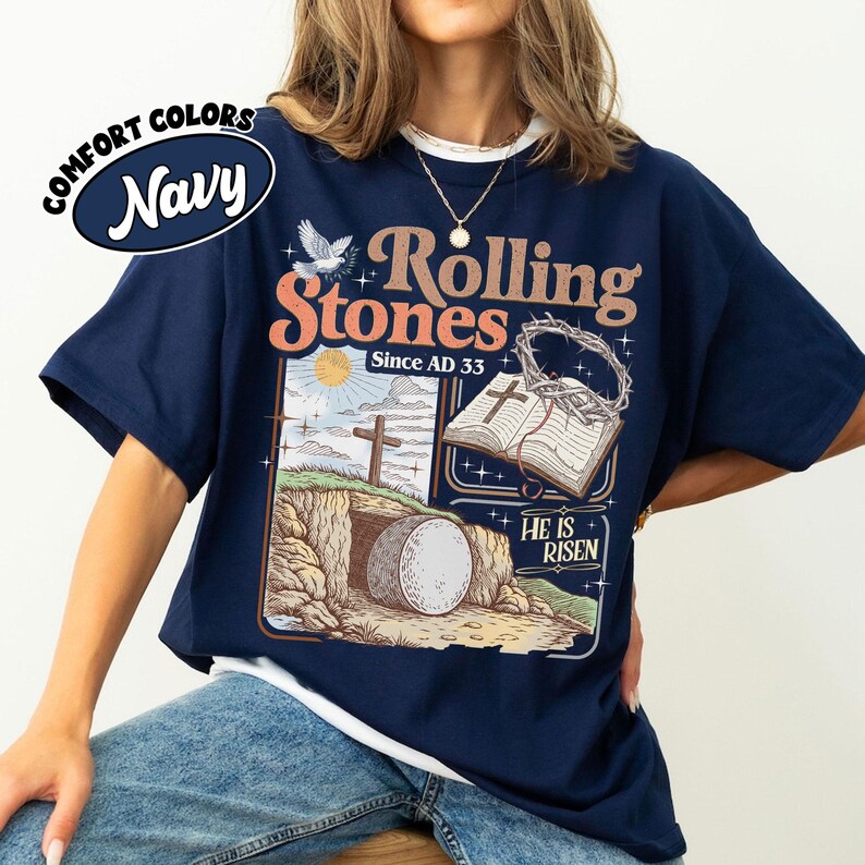 May include: Navy blue t-shirt with a graphic featuring the text "Rolling Stones Since AD 33" and an illustration of a religious scene with a tomb, cross, and open book. The shirt has a white collar.