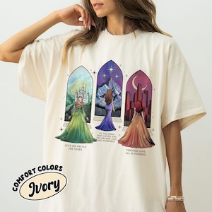 May include: A white t-shirt with a graphic print of three women standing in front of stained glass windows. The text on the shirt reads "Let's go rattle the stars", "To the stars who listen and the dreams that are answered", and "Through love all is possible".