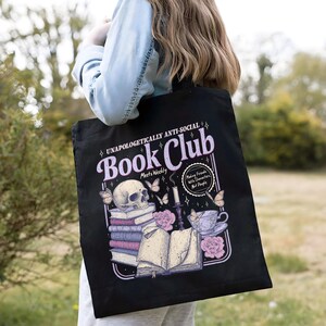 May include: Black tote bag with a graphic design featuring a skull, books, butterflies, and the text "UNAPOLOGETICALLY ANTI-SOCIAL Book Club". The design includes the phrase "Making Friends With Characters, Not People".