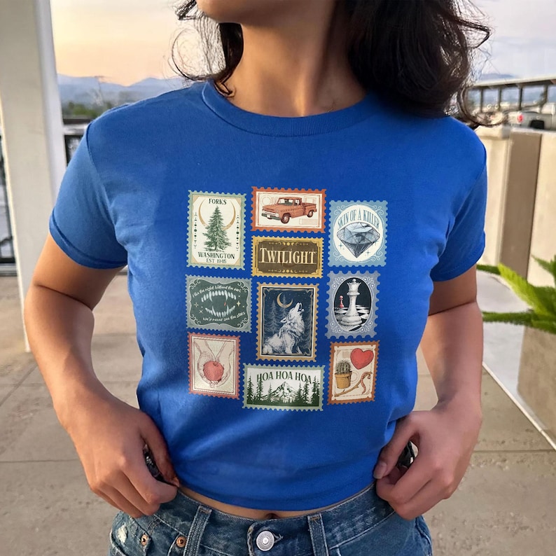 May include: Royal blue t-shirt featuring a collection of postage stamp designs. The stamps depict various images, including a truck, a wolf, a lighthouse, and the word "Twilight". The shirt is a crew neck style.