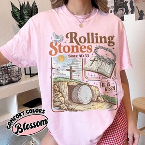 May include: Pink Comfort Colors t-shirt with a graphic featuring the words "Rolling Stones Since AD 33". The graphic includes a dove, cross, open book, and a tomb with the words "He is Risen".