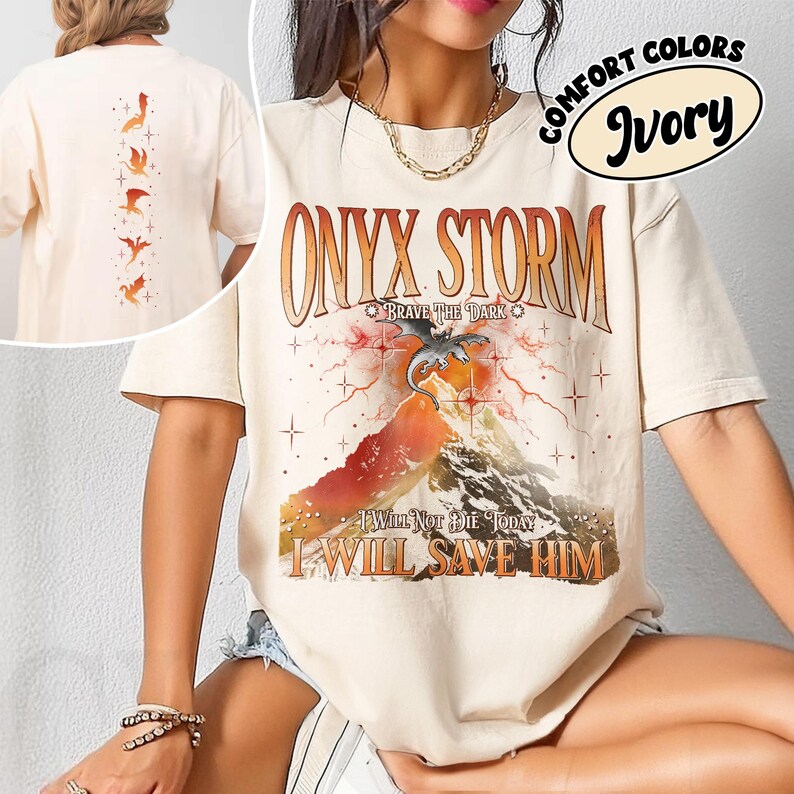 May include: Ivory-colored t-shirt with the text "ONYX STORM" and a graphic of a mountain, dragon, and lightning. The shirt also features the phrases "BRAVE THE DARK", "I WILL NOT DIE TODAY", and "I WILL SAVE HIM". The back of the shirt has a design of birds.