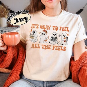 May include: A white t-shirt with the text "It's okay to feel all the feels" in orange lettering. Four cartoon ghosts are holding books with the text "It's okay to feel all the feels" in orange lettering.