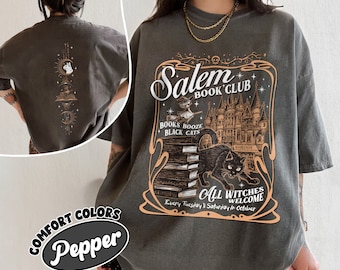 Könnte beinhalten: Ein dunkelgraues T-Shirt mit einem grafischen Aufdruck eines schwarzen Katers, der auf einem Stapel Bücher vor einem Schloss sitzt. Der Aufdruck enthält auch den Text "Salem Book Club", "Books Booze Black Cats" und "All Witches Welcome Every Tuesday & Saturday in October".