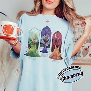 May include: A light blue t-shirt with a graphic of three women standing in front of stained glass windows. The text on the shirt reads "Let's go battle the stars", "To the stars who listen and the dreams that are answered", and "Through love all is possible".