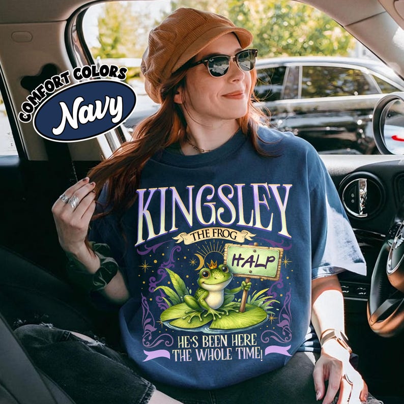 Puede incluir: Camiseta azul marino con un gr&aacute;fico de una rana llamada Kingsley sosteniendo un letrero que dice "HALP". La camiseta tambi&eacute;n presenta el texto "He's Been Here The Whole Time!" y "Comfort Colors Navy".