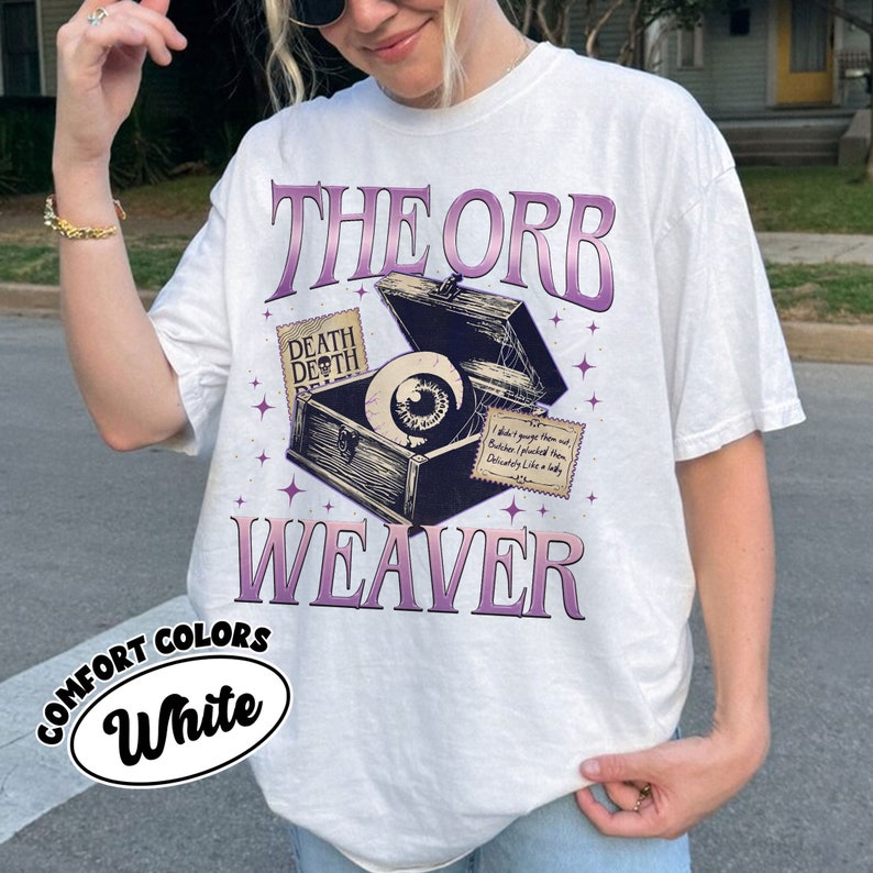 May include: White t-shirt with a graphic of a vintage wooden box with an eye inside. The text "THE ORB WEAVER" is printed in purple on the shirt. The text "DEATH DEATH" is printed on a small tag attached to the box.