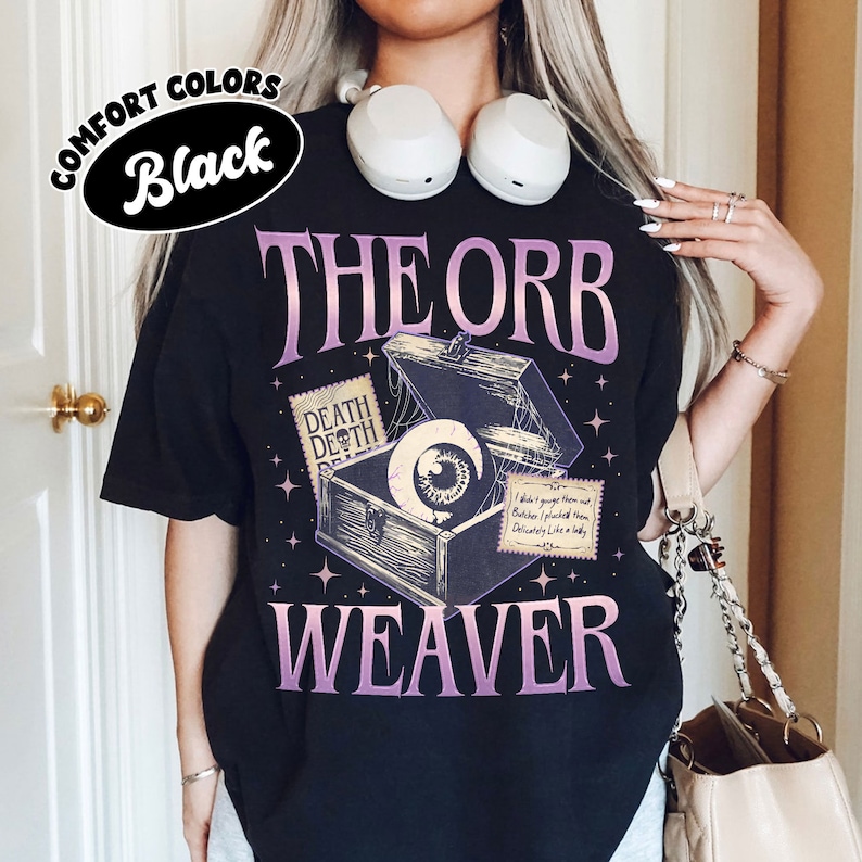 May include: Black t-shirt with a graphic of an eye in a wooden box with the text "The Orb Weaver" in purple.