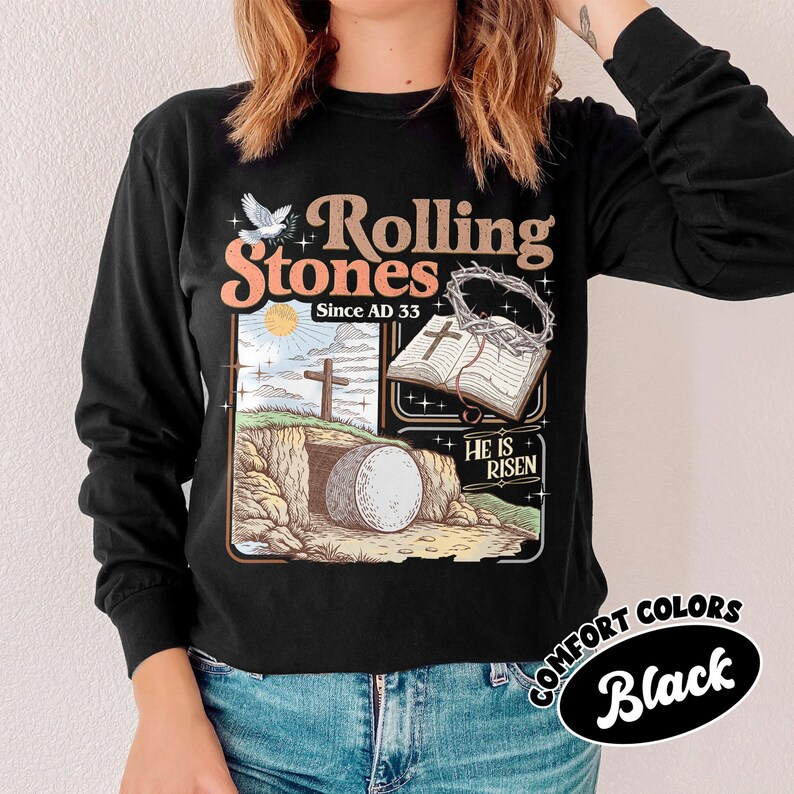 May include: Black long-sleeve shirt with a graphic featuring the text "Rolling Stones Since AD 33" and an illustration of a cross, open book, and empty tomb. The shirt has a round Comfort Colors label in the bottom right corner.