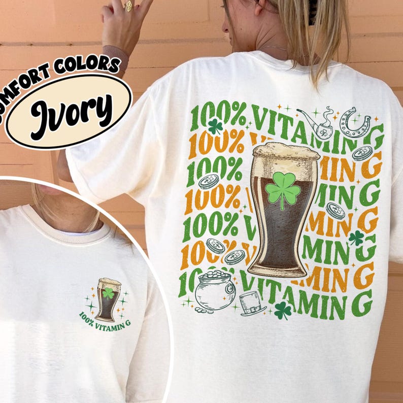 May include: Cream-coloured t-shirt with a St. Patrick's Day design. The back displays a beer glass with a shamrock, text reading "100% Vitamin G", and related graphics. The front has a smaller version of the beer glass graphic.
