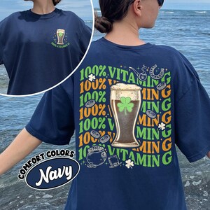 May include: Navy blue t-shirt with a graphic of a beer glass with a shamrock and the text "100% Vitamin G". The shirt also features the text "Comfort Colors Navy".