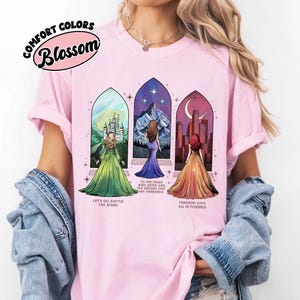 May include: Pink t-shirt with a graphic of three women standing in front of stained glass windows. The text on the shirt reads "Let's go rattle the stars", "To the stars who listen and the dreams that are answered", and "Through love all is possible".