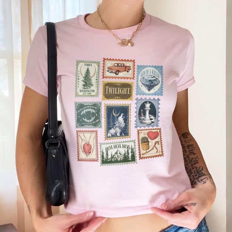 May include: A light pink t-shirt featuring a collage of postage stamp designs. The stamps depict various images, including a truck, a diamond, a wolf, and the word "Twilight". The shirt has short sleeves and a crew neck.