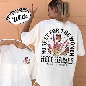 May include: White Comfort Colors t-shirt with a graphic on the back that says "NO REST FOR THE WOMEN HELL RAISER" with a skeleton hand, butterflies, and lightning bolts. The front of the shirt has a smaller matching graphic.