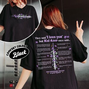May include: Black t-shirt with a floral and sword design on the front and back. The back of the shirt features text that reads "They said 'I love you' but Kai Azer once said..." and a list of quotes. The shirt is labeled "Comfort Colors."