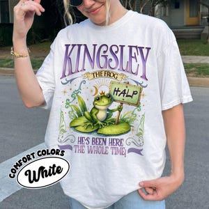 Puede incluir: Camiseta blanca con un gr&aacute;fico de una rana con corona, sosteniendo un letrero que dice "HALP". La camiseta presenta el texto "KINGSLEY THE FROG" en morado, con la frase "HE'S BEEN HERE THE WHOLE TIME" debajo de la rana. La camiseta tambi&eacute;n tiene las palabras "COMFORT COLORS" y "White".