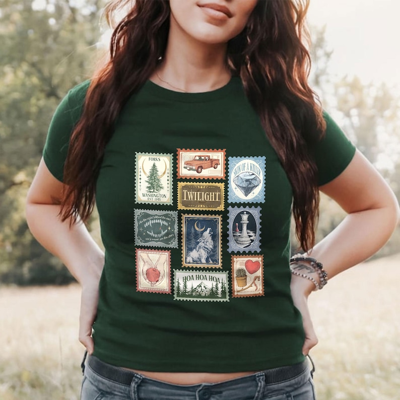 May include: Dark green t-shirt featuring a collection of postage stamp designs. The stamps depict various images, including a pine tree, a red truck, a wolf, and the word "TWILIGHT".